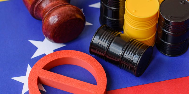 Metal barrels of oil, gas, or chemicals bearing on the flag of venezuela and a ban sign, embargo on venezuelan production. Barrels of Iranian oil